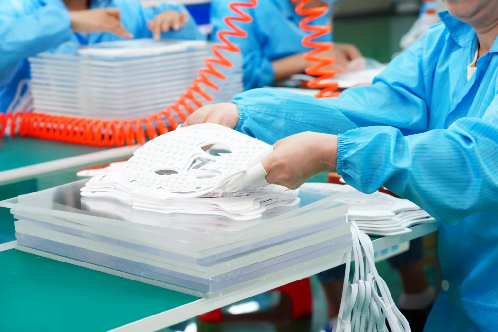 Workers assembling medical-grade LED face masks in a cleanroom production line at a light therapy device factory