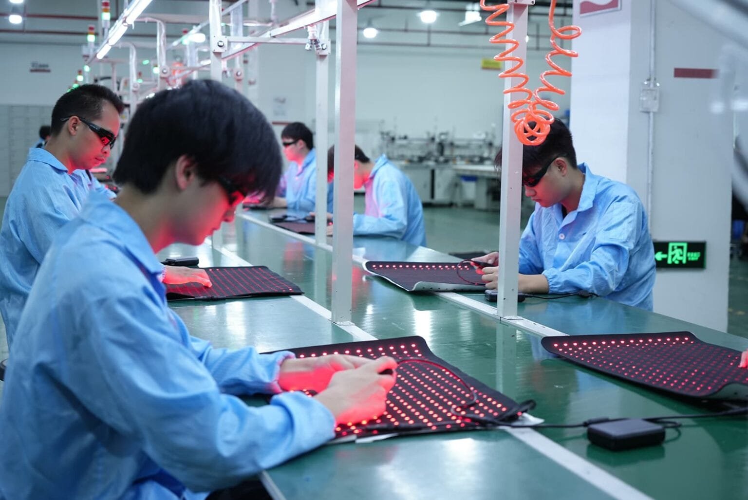 Línea de producción de almohadillas de terapia de luz roja para mascotas con trabajadores que prueban paneles de luz LED