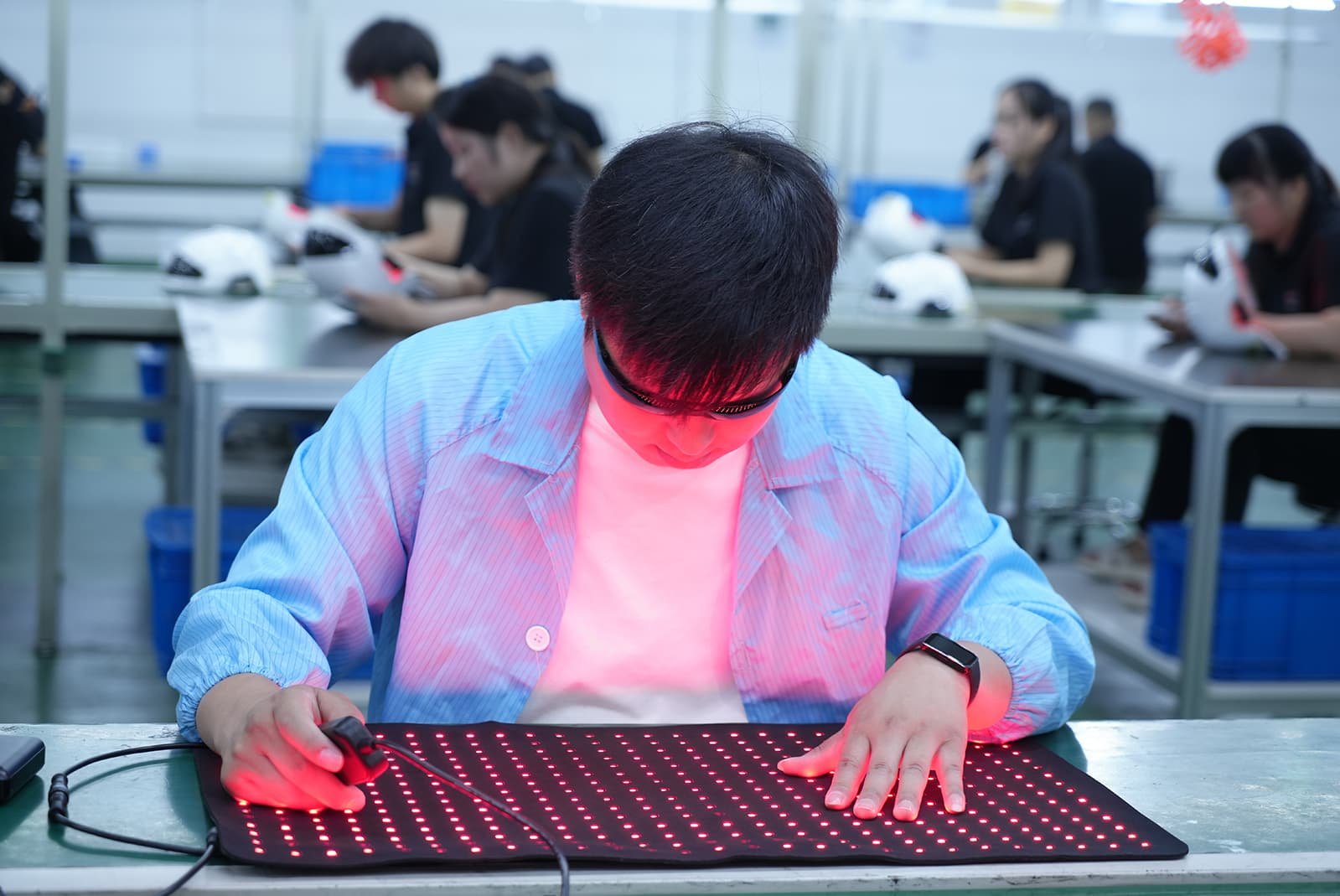 Factory worker inspecting a pet red light therapy pad on the LED production line in a medical-grade manufacturing facility.